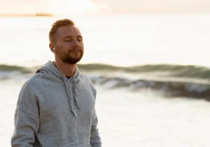 Mindfullness redusere angst og depresjon – Mann med lukkede øyne nyter havbrisen, en rolig stund for mental velvære. Besøk psykiater.no.
