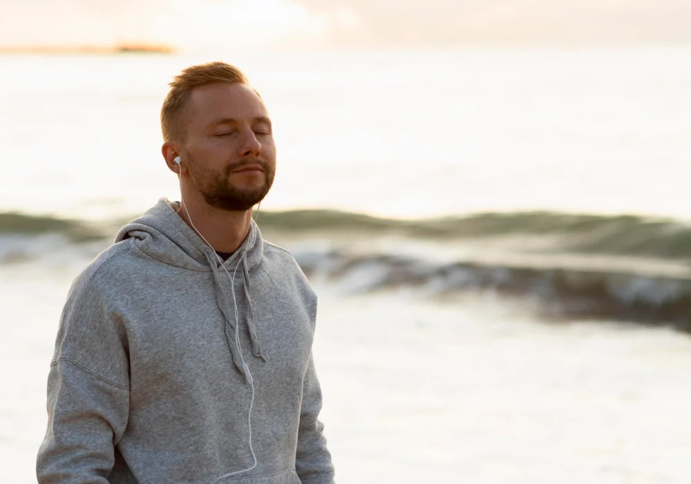 Mindfullness redusere angst og depresjon – Mann med lukkede øyne nyter havbrisen, en rolig stund for mental velvære. Besøk psykiater.no.