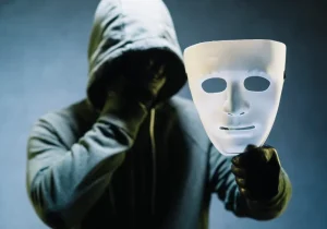 Person iført en hettegenser som holder en maske foran ansiktet – symbolsk bilde som illustrerer den skjulte smerten ved maskert depresjon.