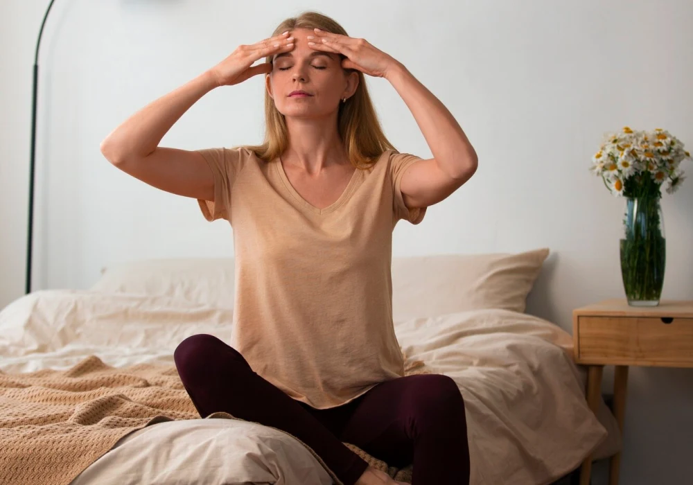 Kvinne praktiserer morgenmeditasjon på soverommet for å lindre morgendepresjon, sittende i en rolig og avslappet stilling.
