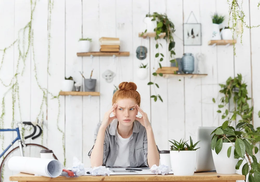 Kvinne med konsentrasjonsvansker og stress på kontoret, omgitt av planter – illustrerer utfordringer ved ADHD på arbeidsplassen.