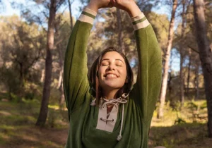 En smilende kvinne strekker seg gledelig i en solfylt skog og utstråler fred og balanse – et inspirerende øyeblikk som reflekterer guddommelig mental helse og indre harmoni.