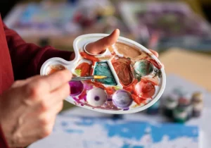 Person som holder en malingspalett med farger og pensel under en kunstøkt, som illustrerer bruken av kunstterapi for psykiske lidelser i behandling og mestring.