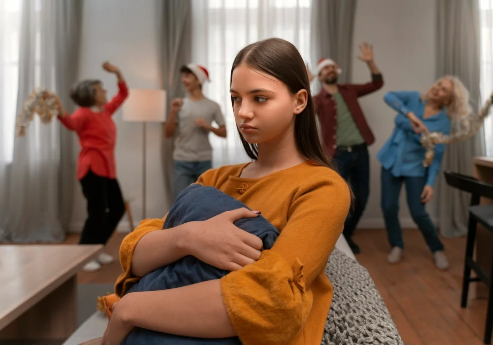 Ung jente føler seg isolert under en fest, mens andre danser i bakgrunnen – illustrasjon av sosial angst og spiseforstyrrelser i sosiale situasjoner.