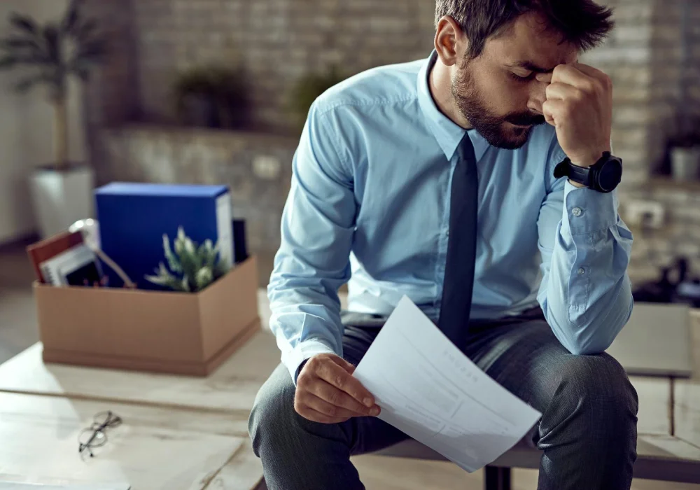 En bekymret mann sitter alene med et papir mens han hviler hodet i hånden, et uttrykk for stress og mental helse i hverdagens utfordringer.