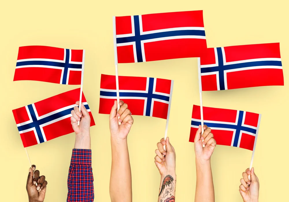 Flere hender holder norske flagg i været mot gul bakgrunn – en illustrasjon av mangfold og nasjonal identitet knyttet til forekomsten av ADHD i Norge.
