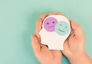 Illustrasjon av følelser i kognitiv terapi – to ansiktsikoner (et nøytralt og et smilende) inni et hode holdt i hender, symboliserer emosjonell bevissthet.