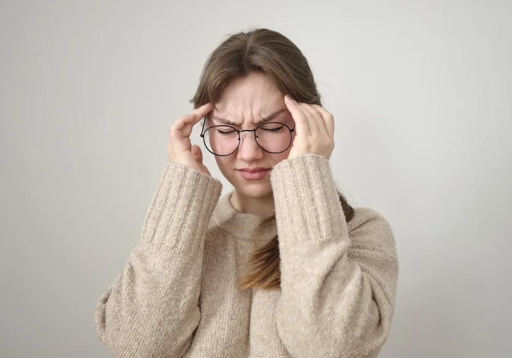 Kvinne med smertefullt uttrykk holder hodet – et bilde som illustrerer sammenhengen mellom migrene og psykiske lidelser som angst og depresjon.