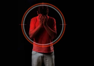 A mann i rødt dekker ansiktet i fortvilelse, omgitt av et målskive-symbol – illustrerer den mørke virkningen av opioid avhengighet og følelsesmessig smerte.