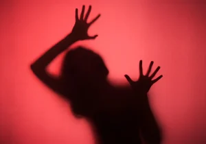 Skyggen av en person med hevede hender mot en rød bakgrunn, som uttrykker intens frykt og fobier i en dramatisk og emosjonell scene.